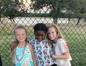 three girls stand together, arms around each other, smiling for a photo