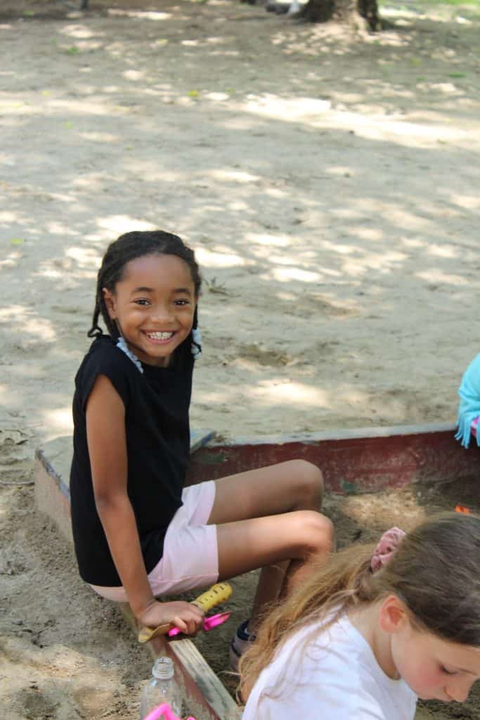 Girls sitting on side of sand box smiling at the camera