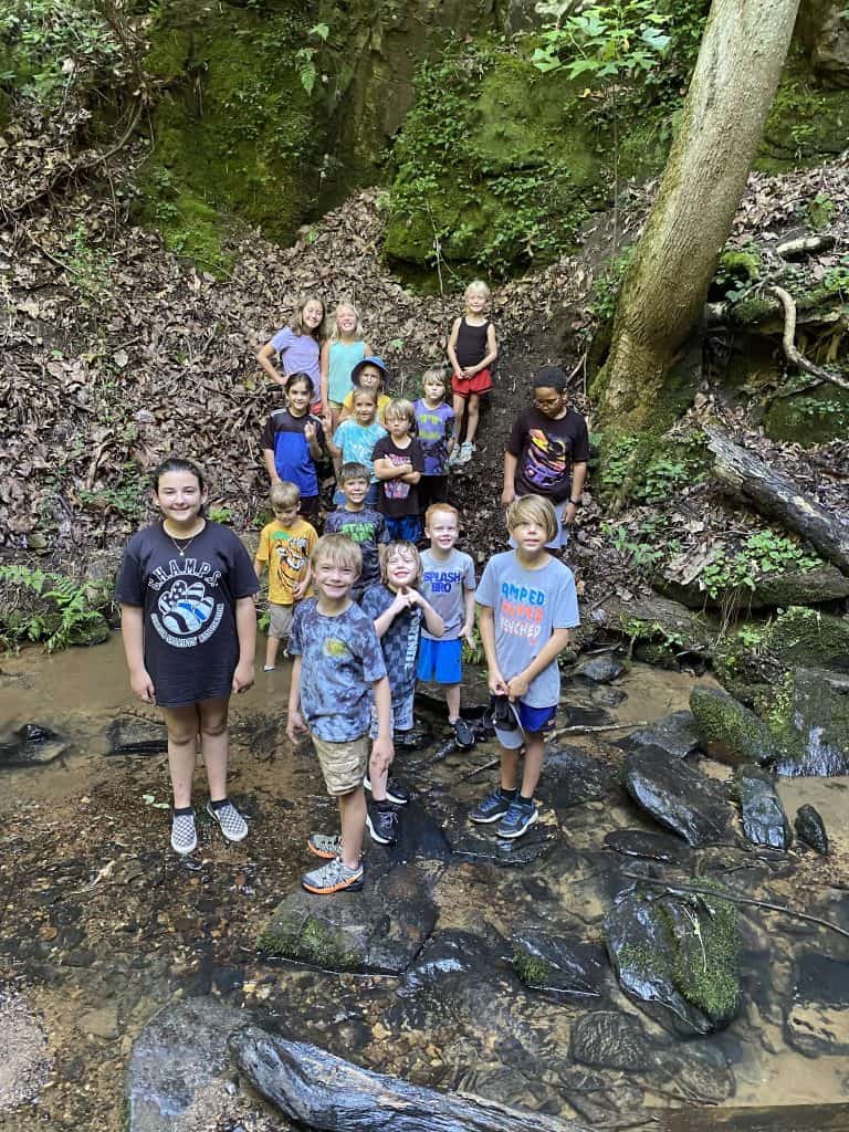 Photo of young people hiking in the woods, crossing a stream, looking up at the camera