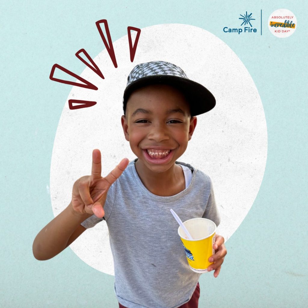 Boy holding ice cream and smiling big, holding up a peace sign with their hand