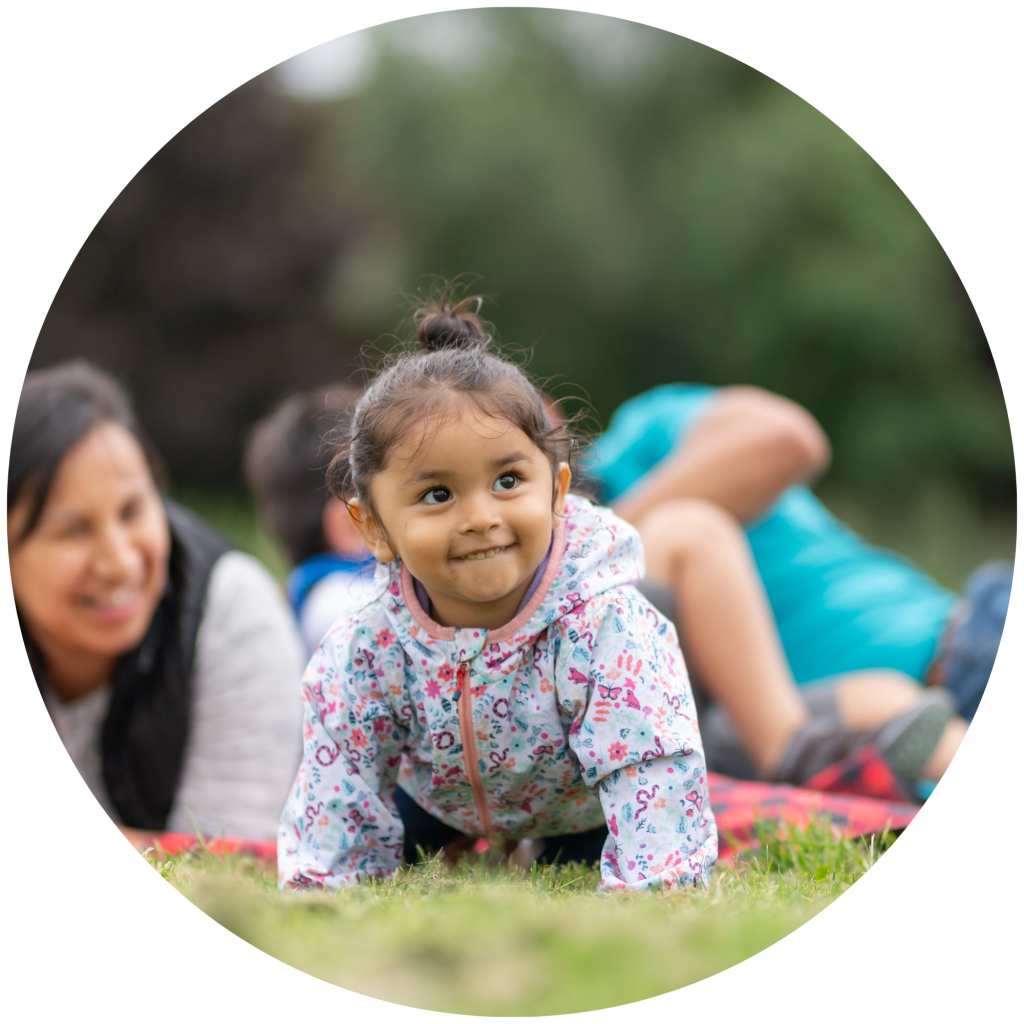 Toddler crawling in the grass with her mom behind her