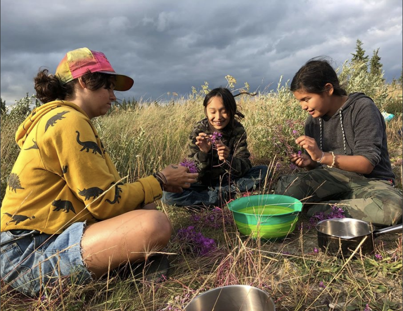 photo of three young people sitting together in a field  collecting flowers